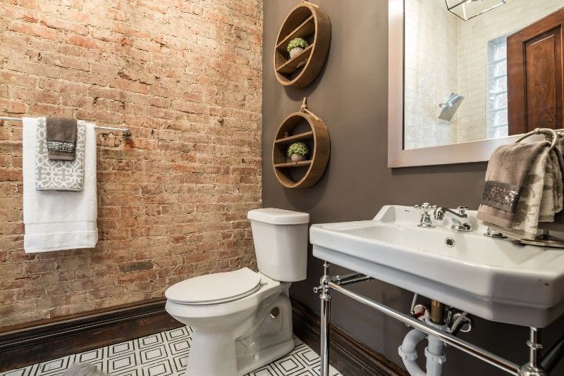 A bathroom with a toilet , sink , mirror and brick wall.