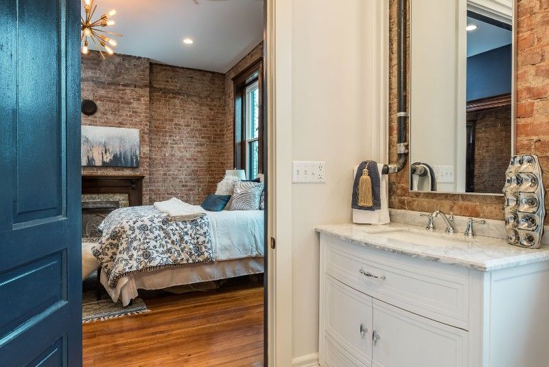 A bathroom with a sink and a mirror next to a bedroom.