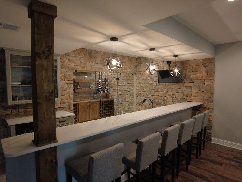 A kitchen with a long counter and stools and a brick wall.