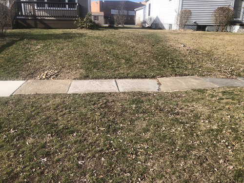 A lawn with a sidewalk and a house in the background.