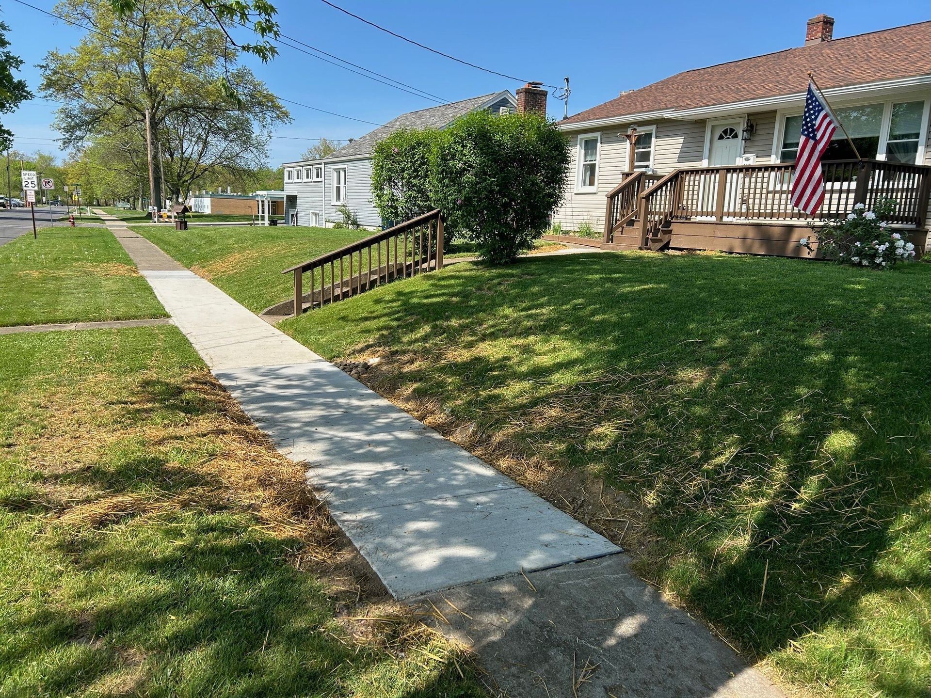 A concrete walkway leading to a house with an American flag on the front porch.