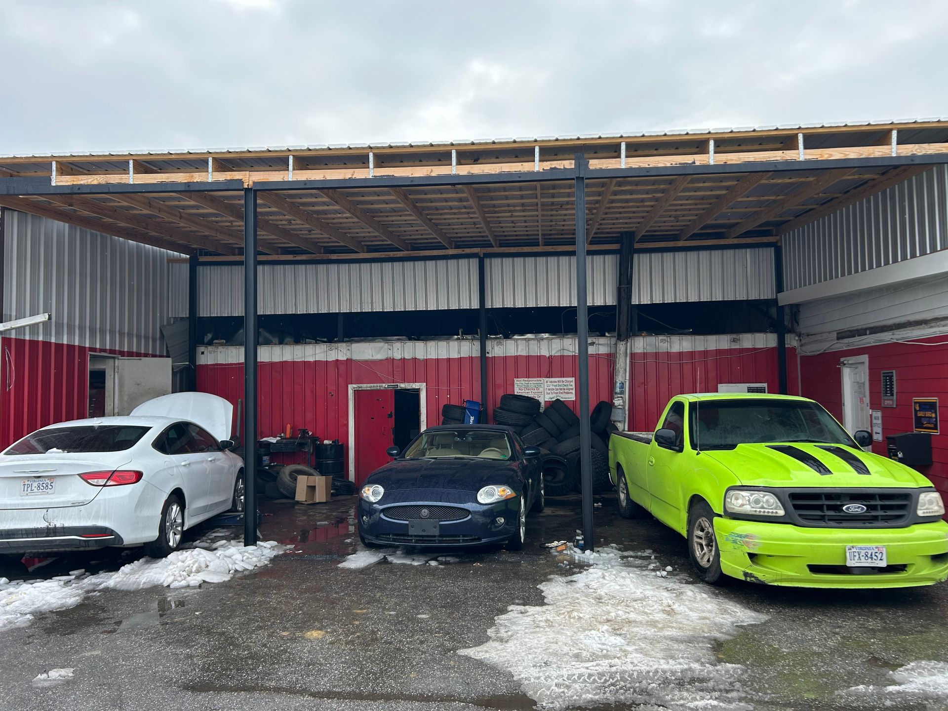 Cars parked under a canopy: white sedan, blue convertible, green pickup. Red building with a snowy ground.