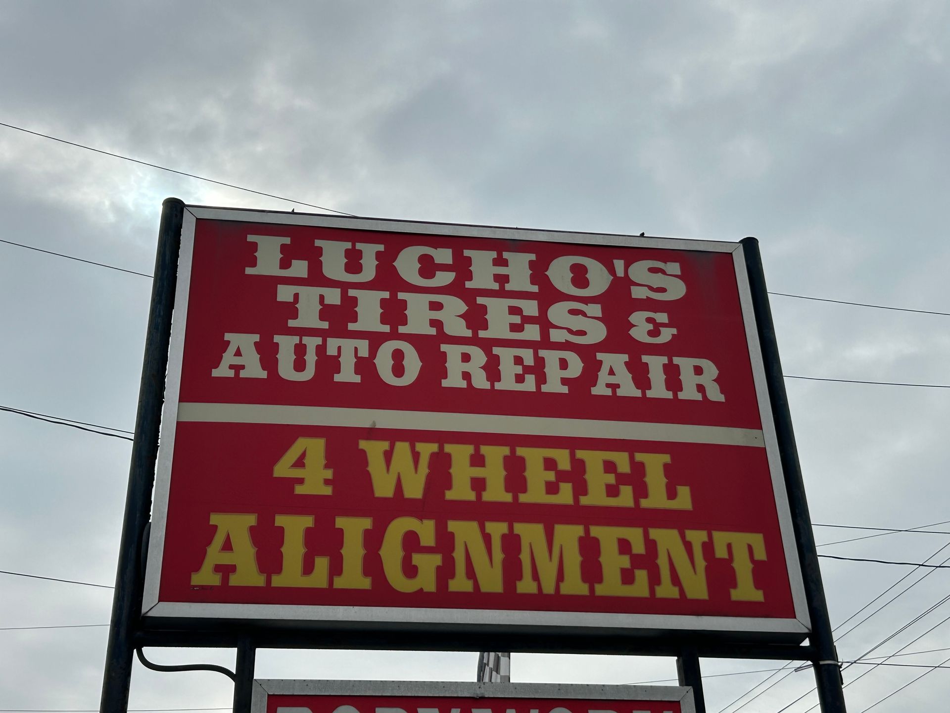 Sign for Lucho's Tires & Auto Repair, red with white and yellow text, cloudy sky background.