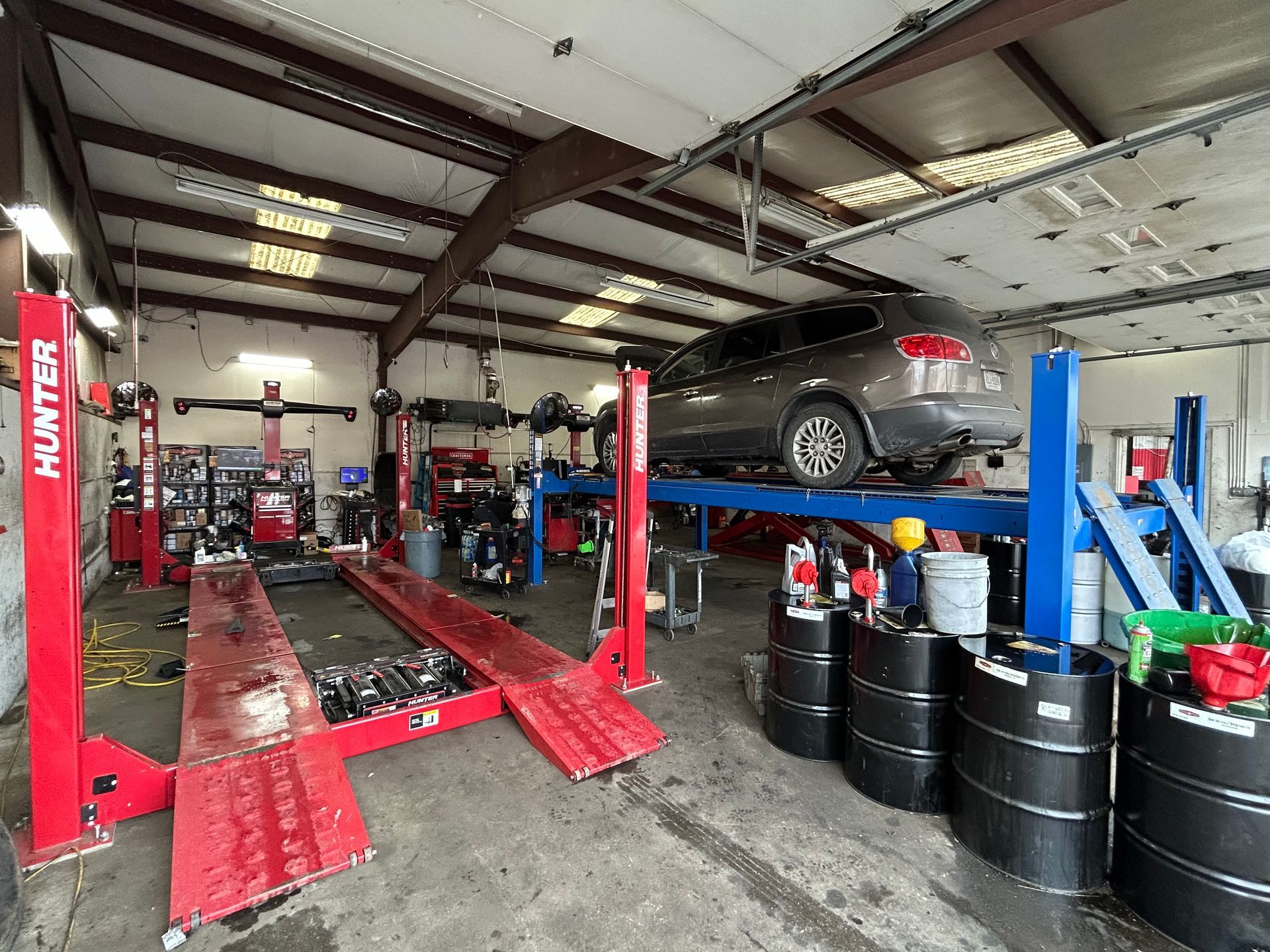 Car on a lift inside a mechanic's garage with red and blue lifts and oil barrels.