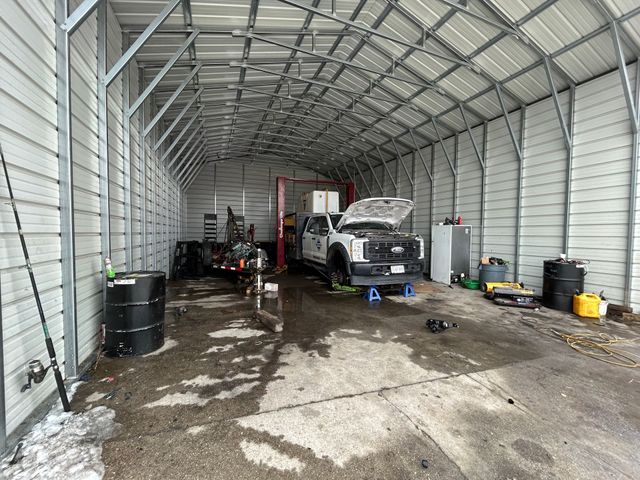 A truck inside a metal garage with the hood open, parked on jack stands.