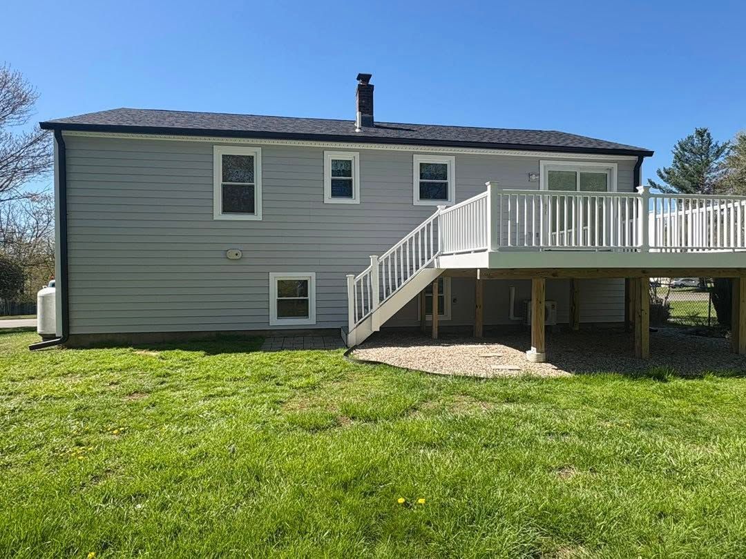 Gray house with white deck stairs and railing over a green lawn under a blue sky