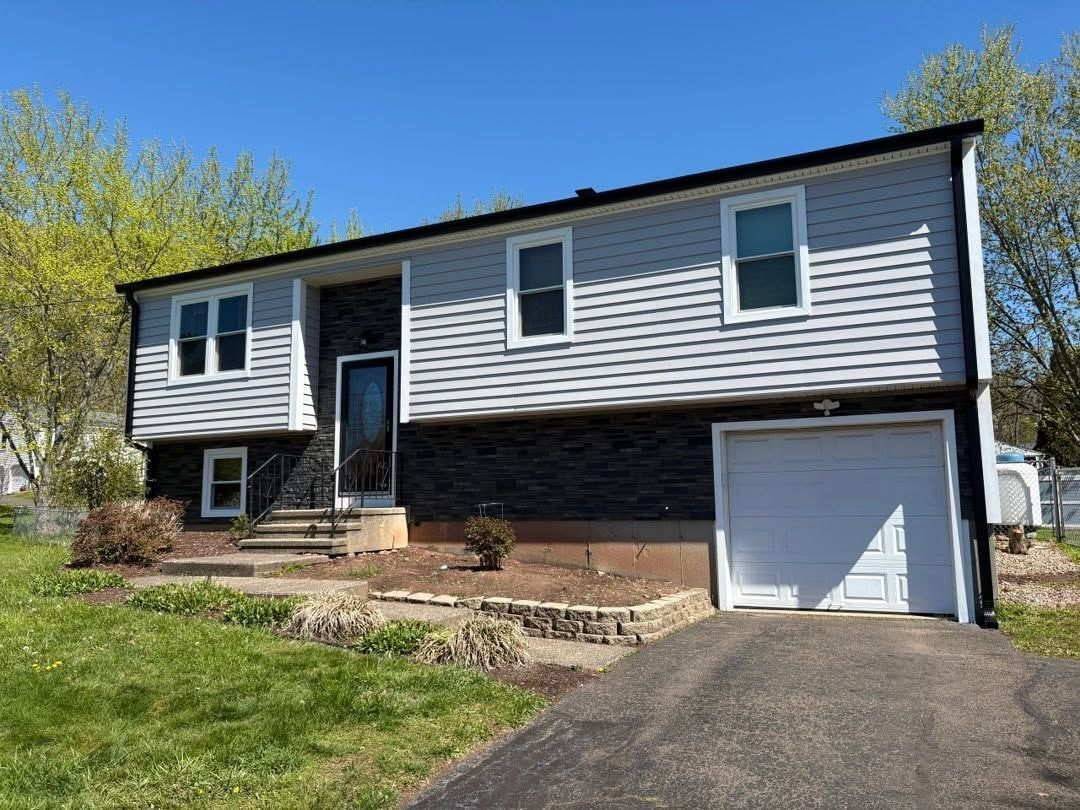 Suburban split-level house with white siding, brick base, front steps, and attached garage under a clear blue sky