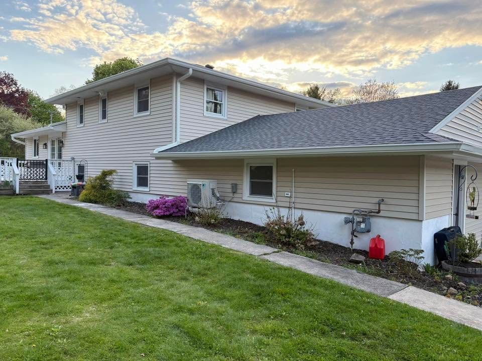 Suburban house with beige siding, gray roof, green lawn, and pink flowers at dusk