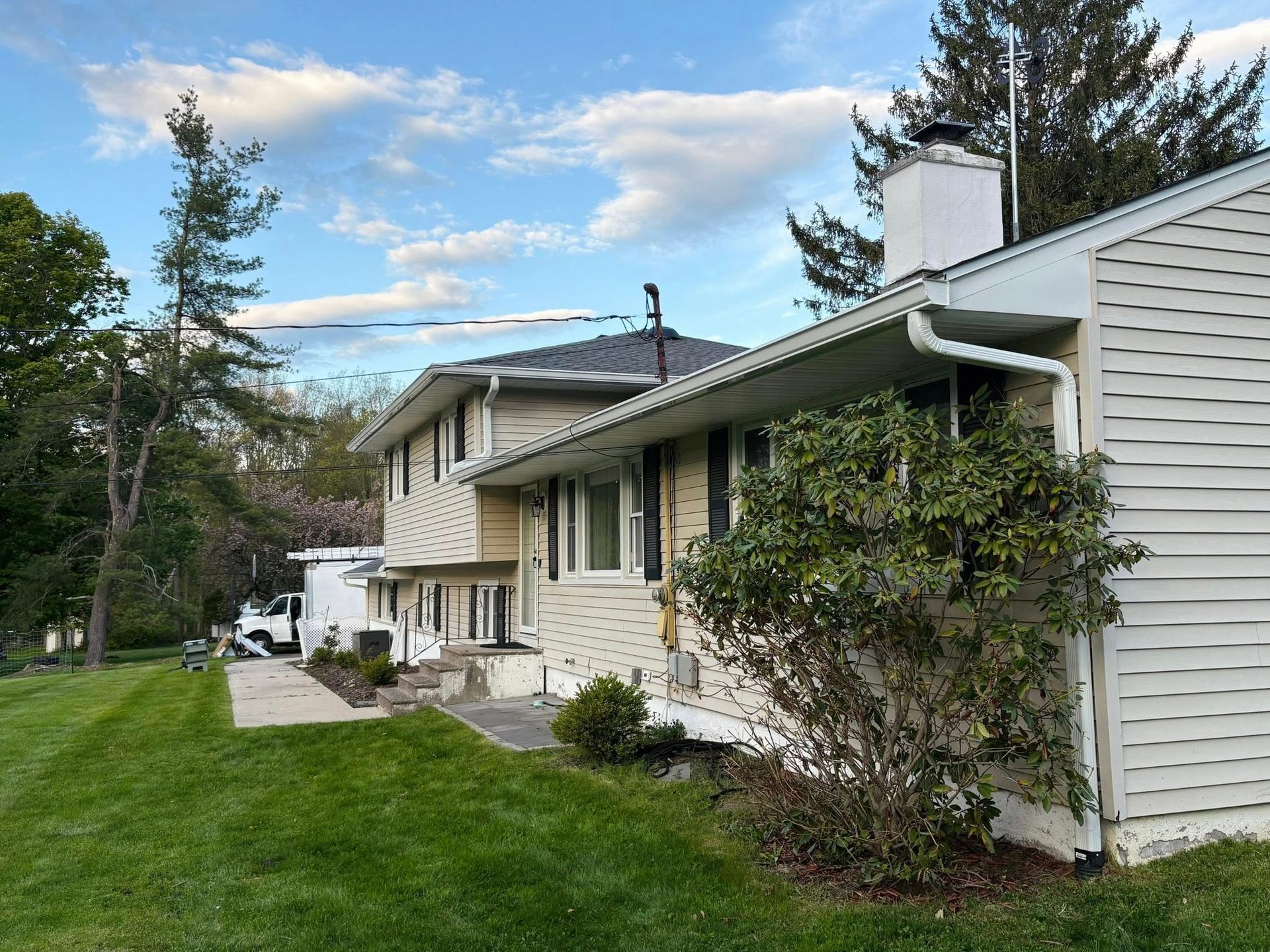 Suburban house with light siding, front porch, and green lawn under a partly cloudy sky