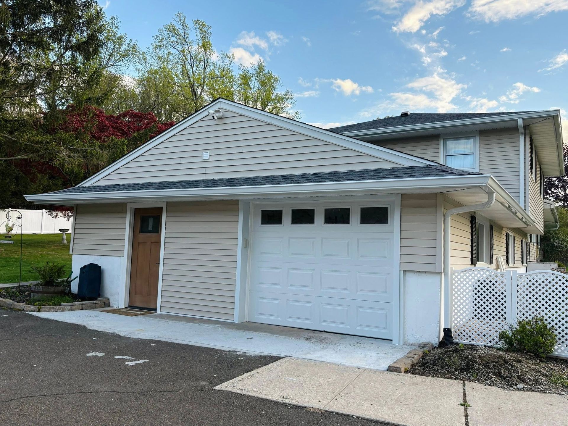 Detached garage with white siding and a single garage door, beige side door, and sloped shingle roof.