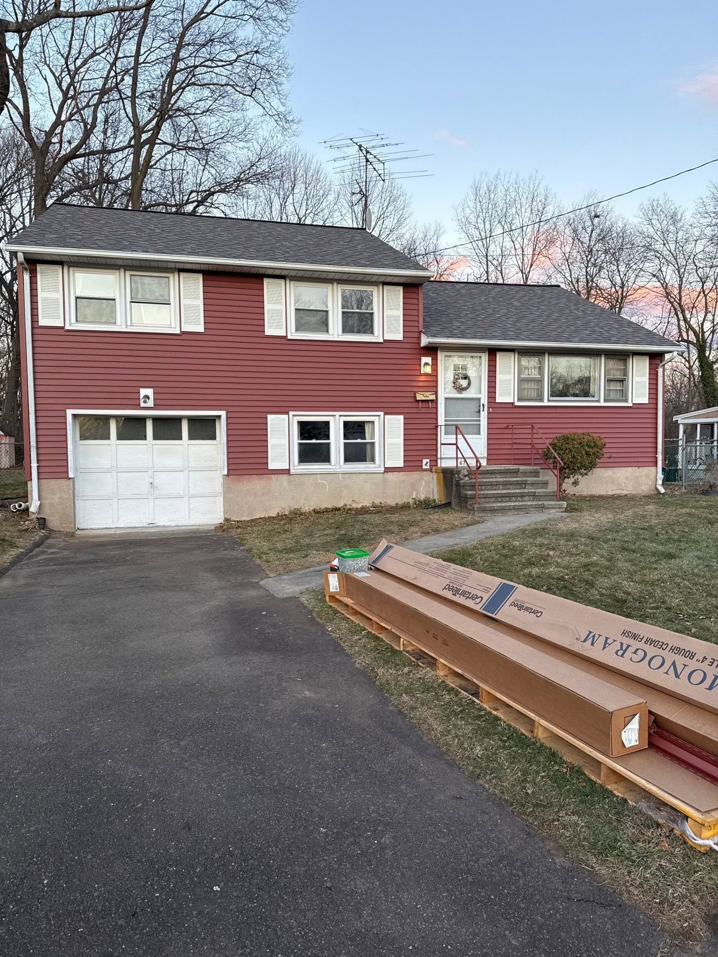 Suburban house with red siding, white garage, driveway, and a large dumpster in front yard.