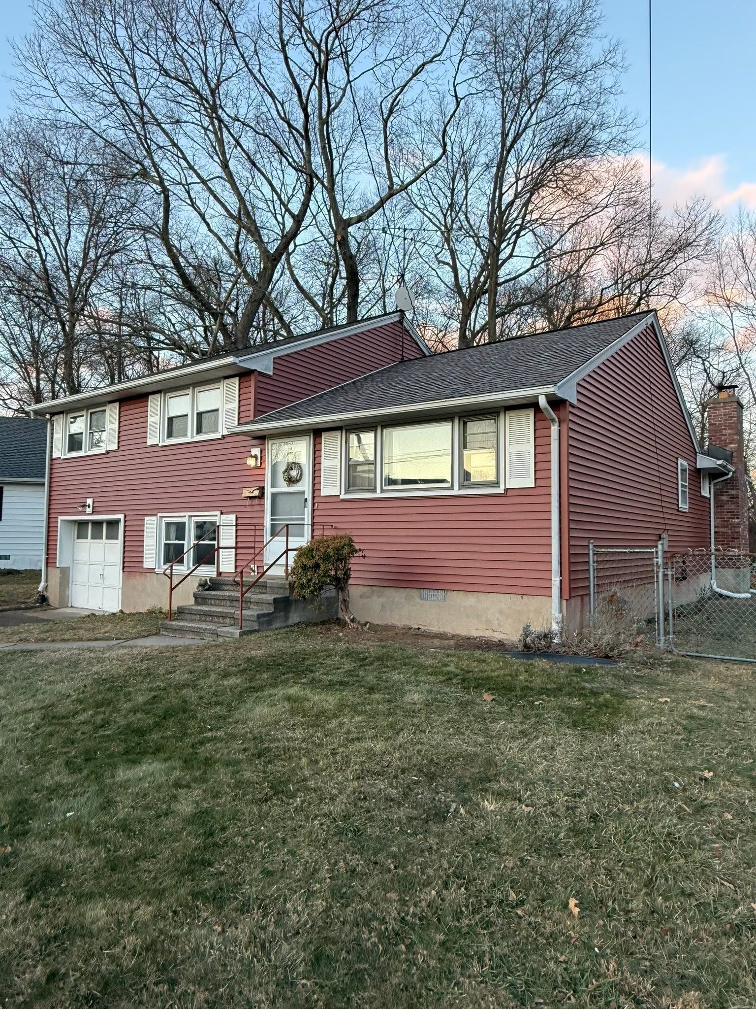 Red two-story house with white trim and a fenced yard at dusk