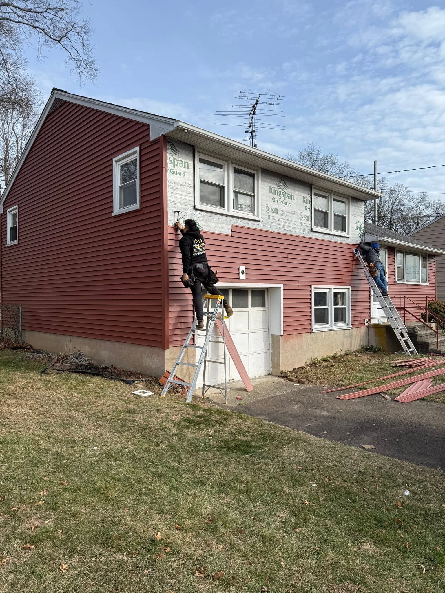Two-story red house with white-trim windows, ladders, and workers painting the exterior.
