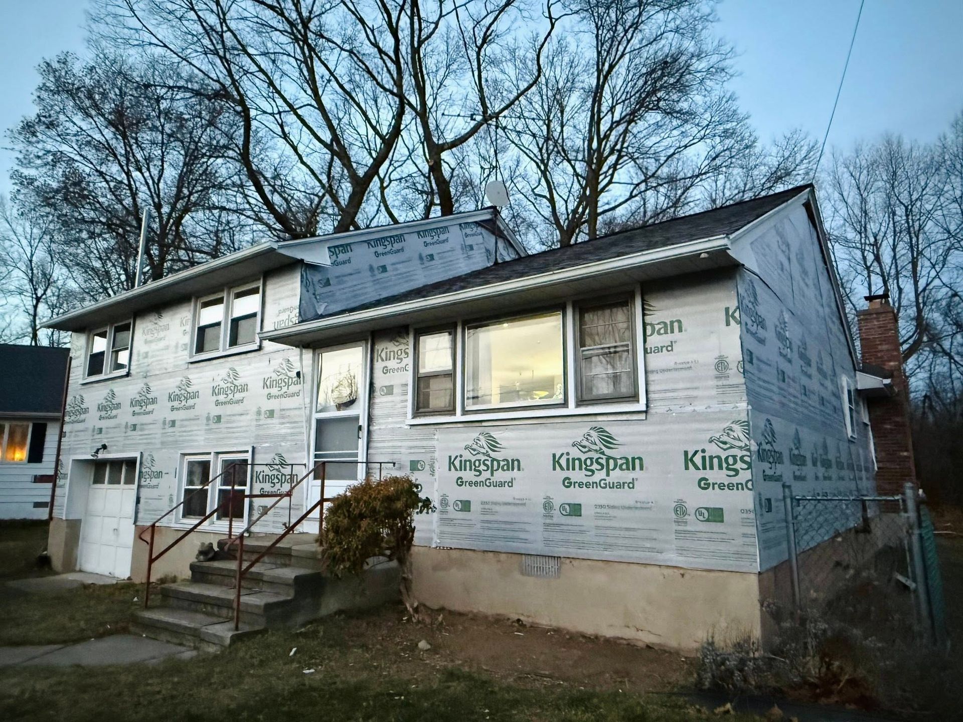 Partially renovated two-story house with white siding and exposed insulation under bare trees
