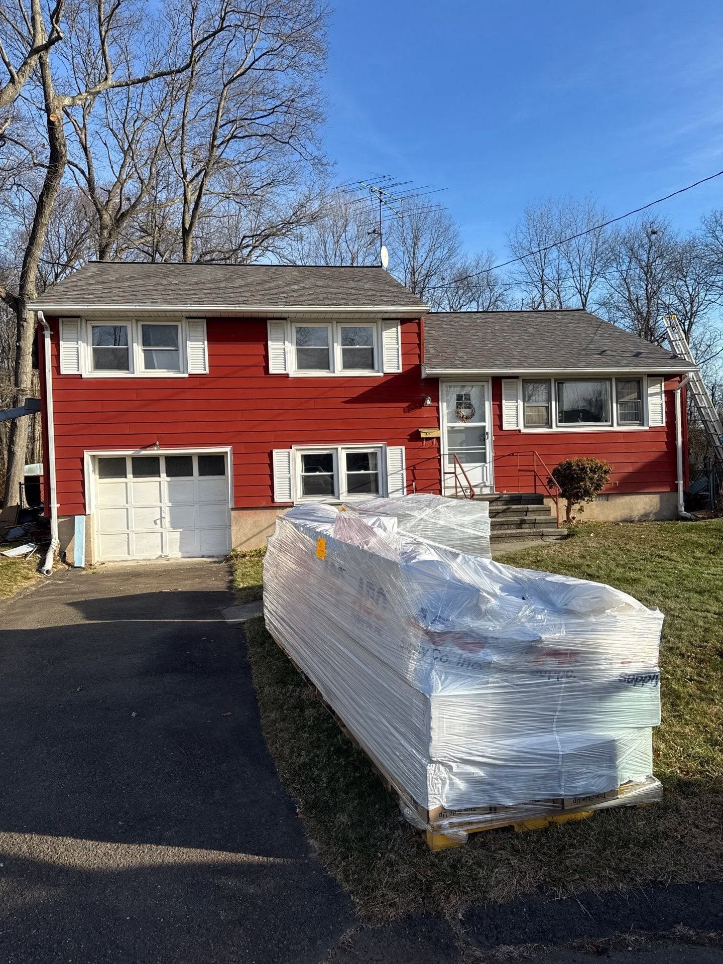Red split-level house with a garage and a large wrapped pallet on the driveway.