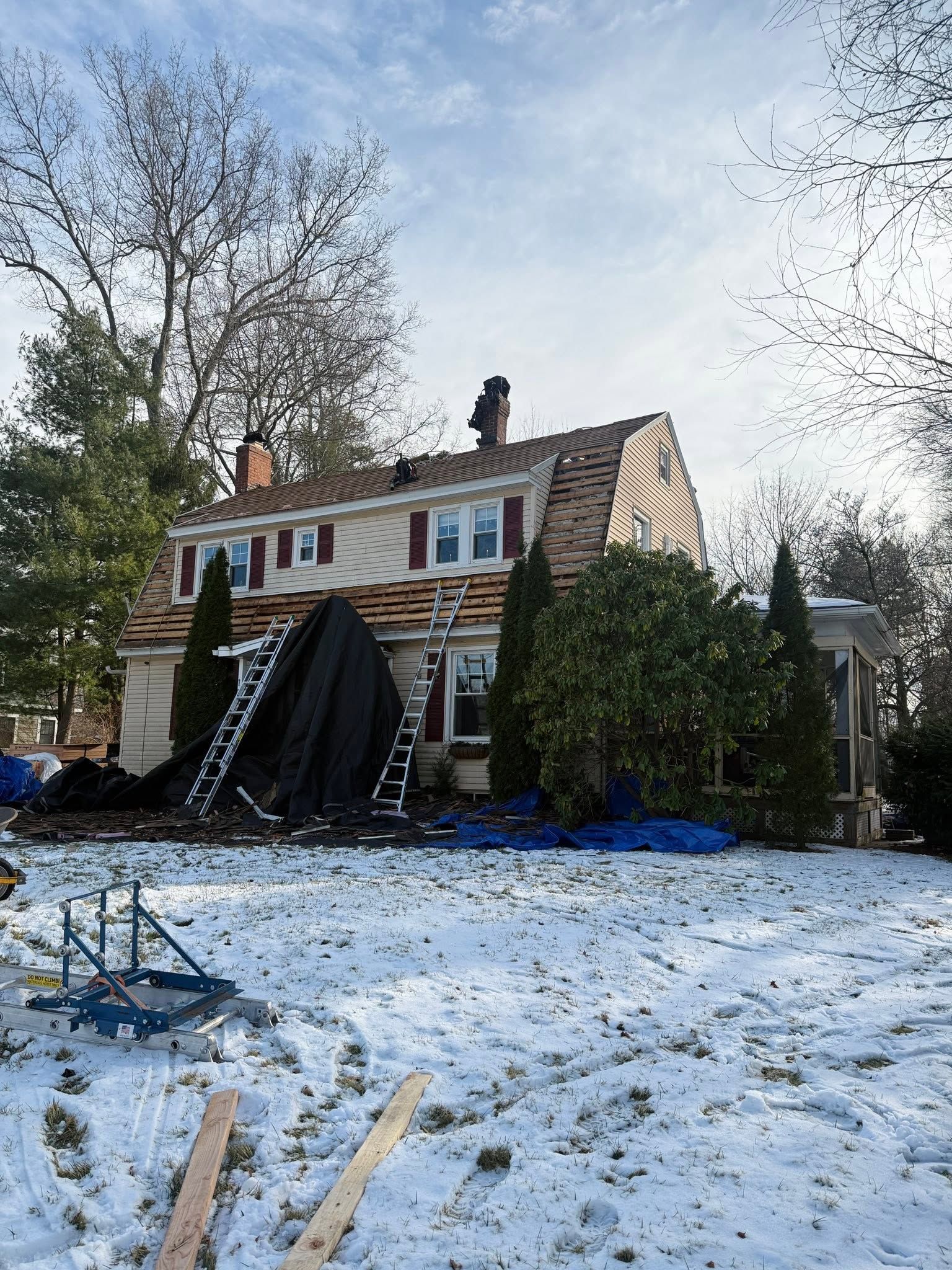 Snow-covered yard with a two-story house and a large black tarp or slide draped over the front.