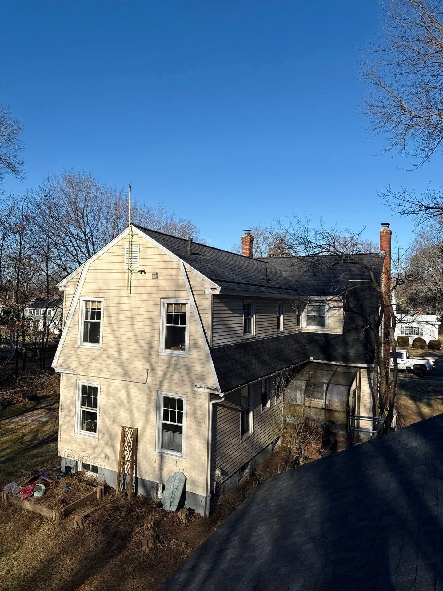 Beige two-story house with dark roof and chimney, viewed from an elevated angle under a clear blue sky