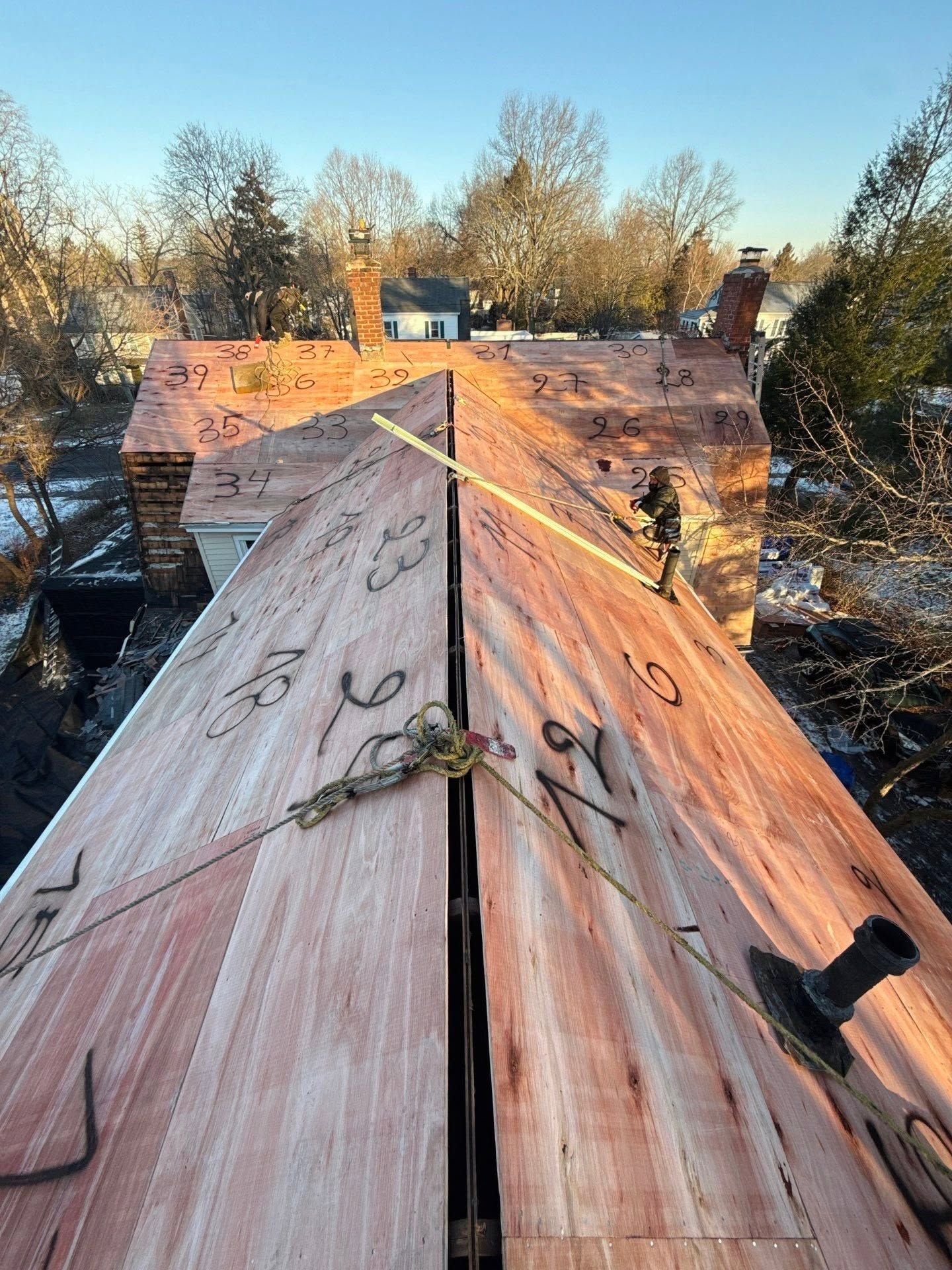 Rooftop under repair with exposed plywood decking, ropes, and trees in the background