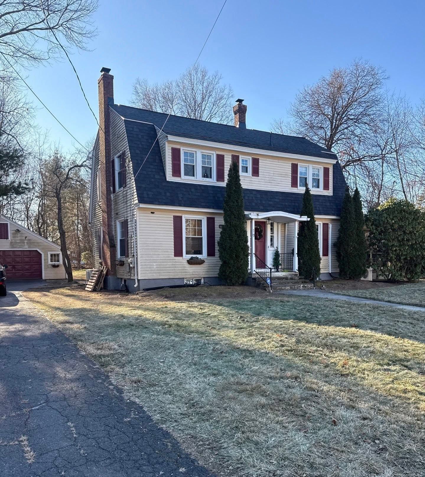Two-story white house with blue roof and red shutters, front porch, and frosty lawn on a sunny day