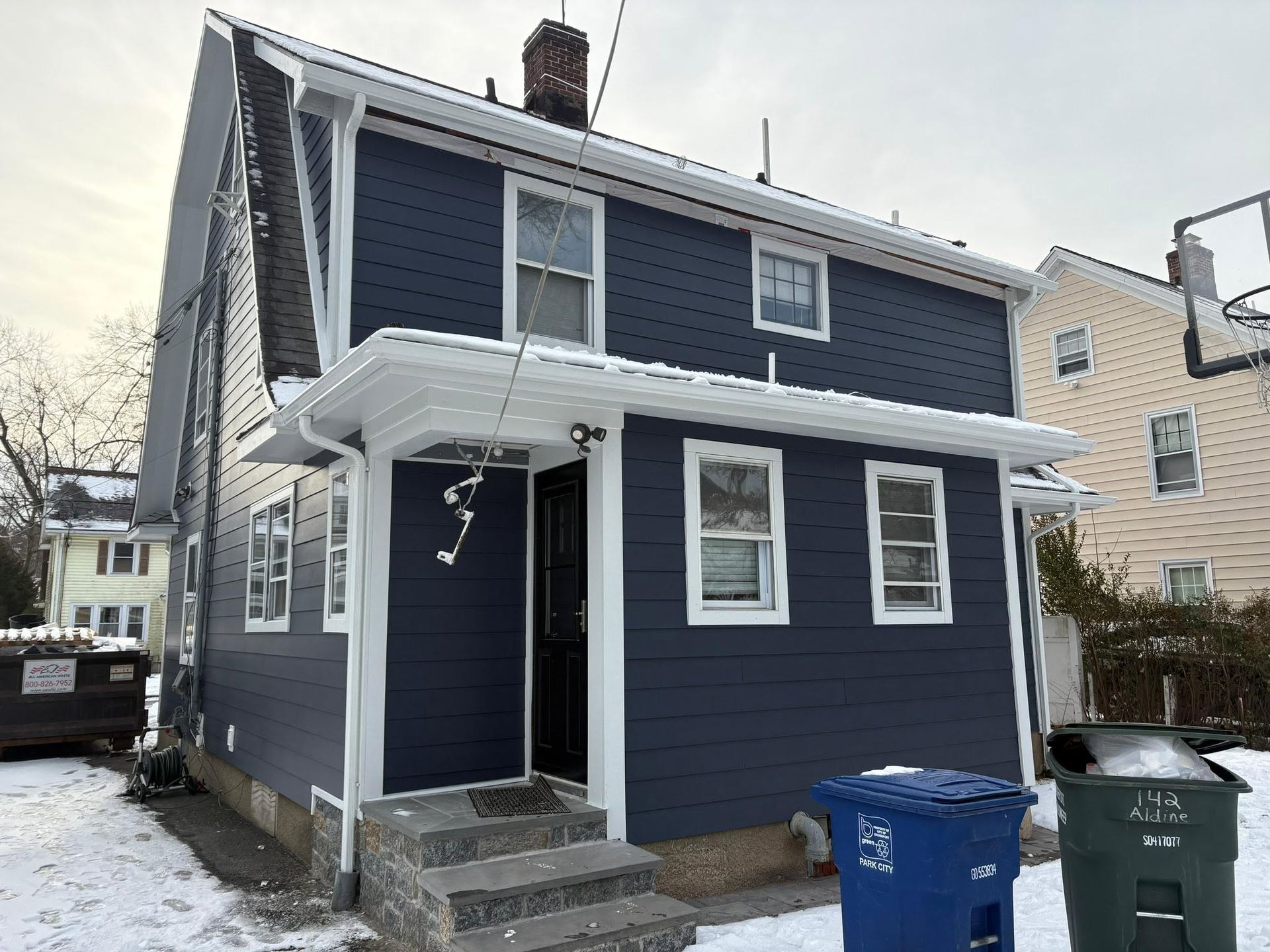 Blue two-story house with white trim and snow-covered steps, seen from the front