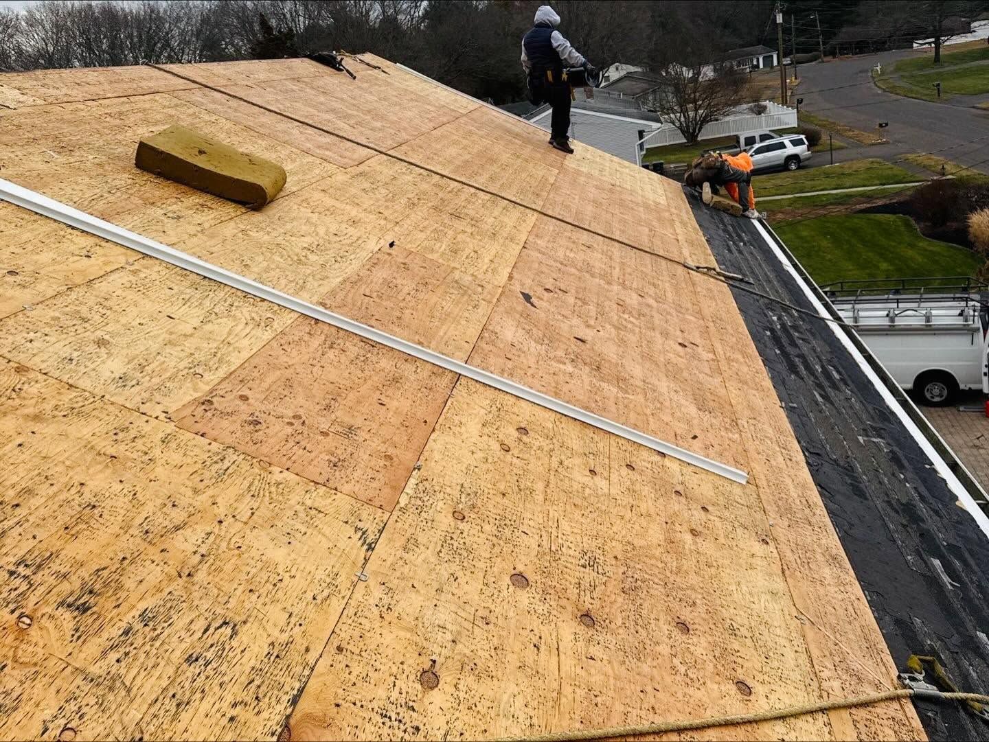 Roof under construction with workers installing plywood sheathing on a sloped roof