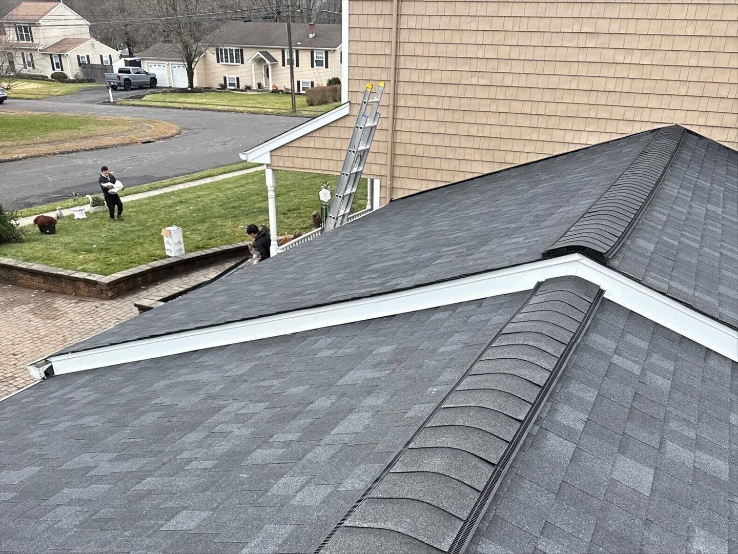 Residential rooftops and chimney in a suburban neighborhood, with a black roof in the foreground.