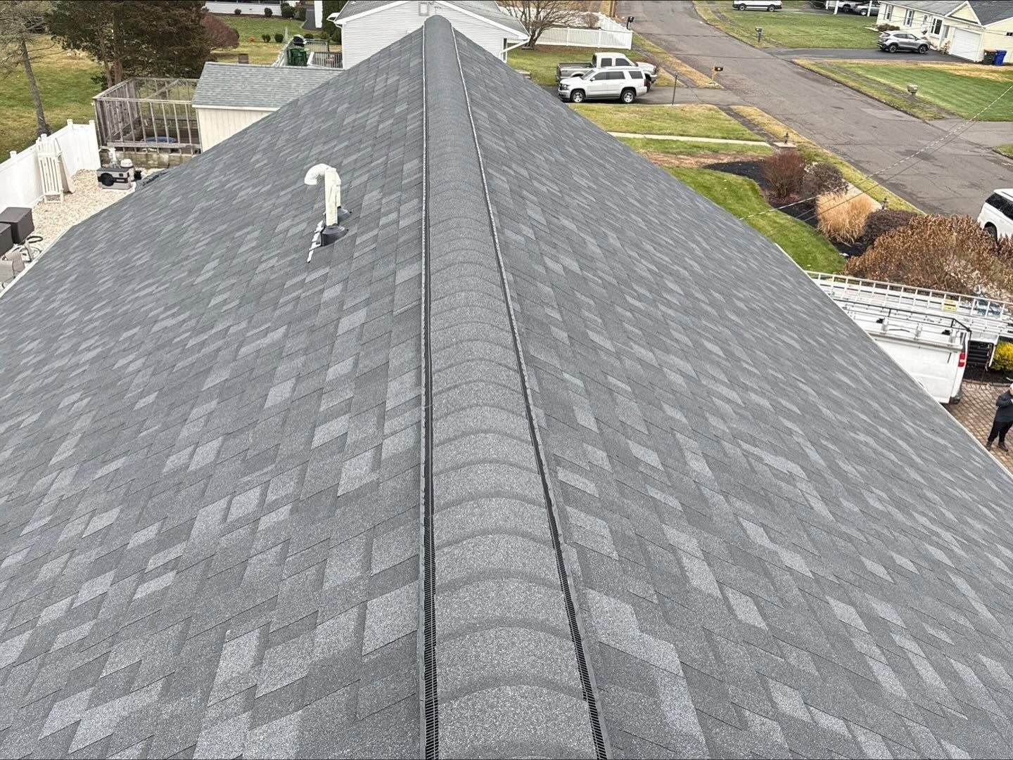 Aerial view of a gray shingled roof with a vent, driveway, and street visible around it.