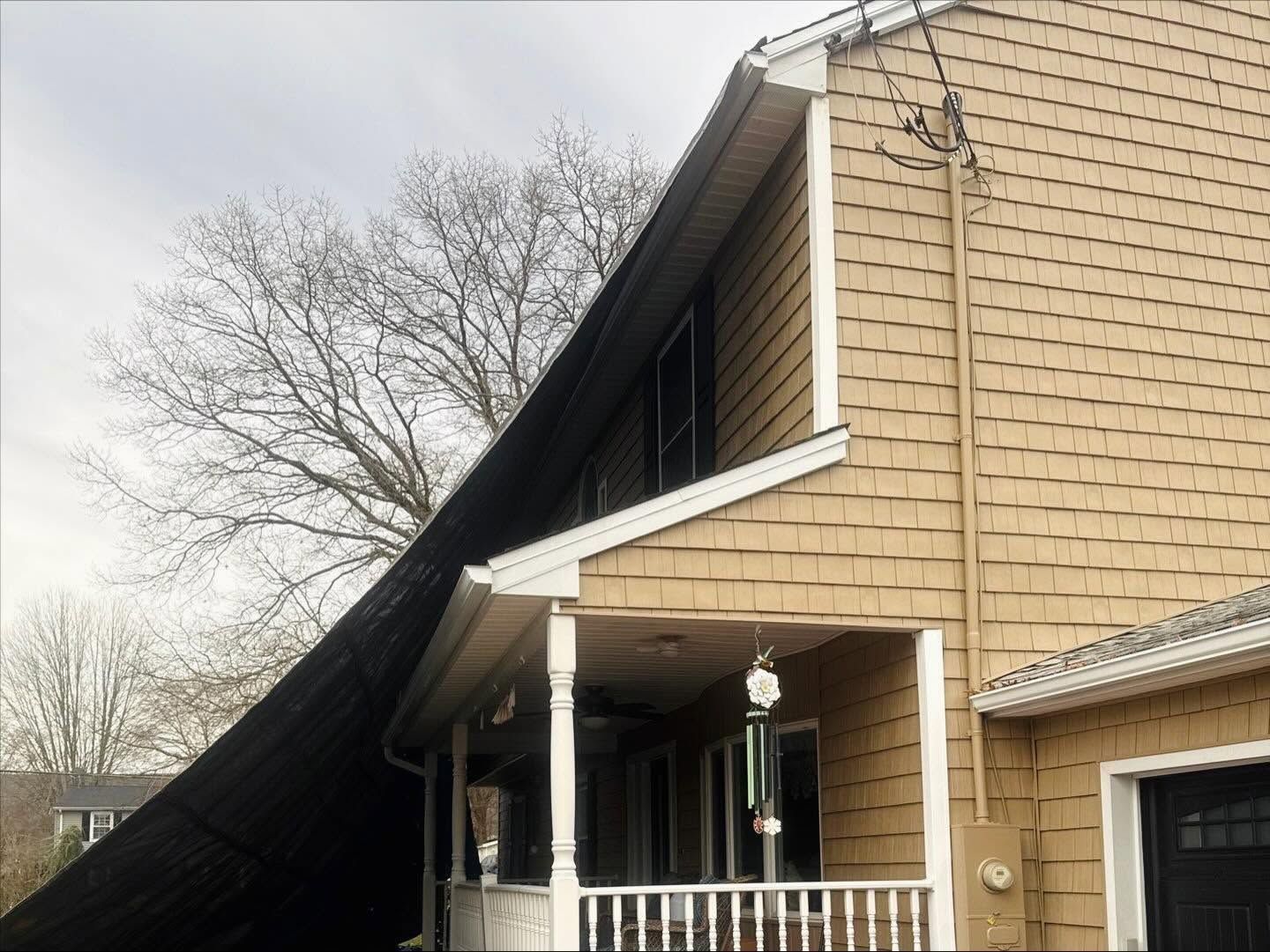 Large dark tarp draped over a house roof and front porch, with damaged siding visible
