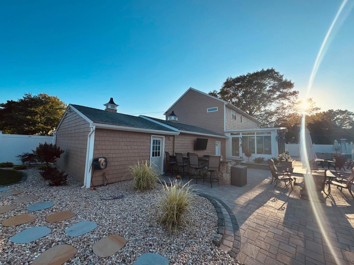 Sunny backyard patio with stone pavers, chairs, and a house at sunset