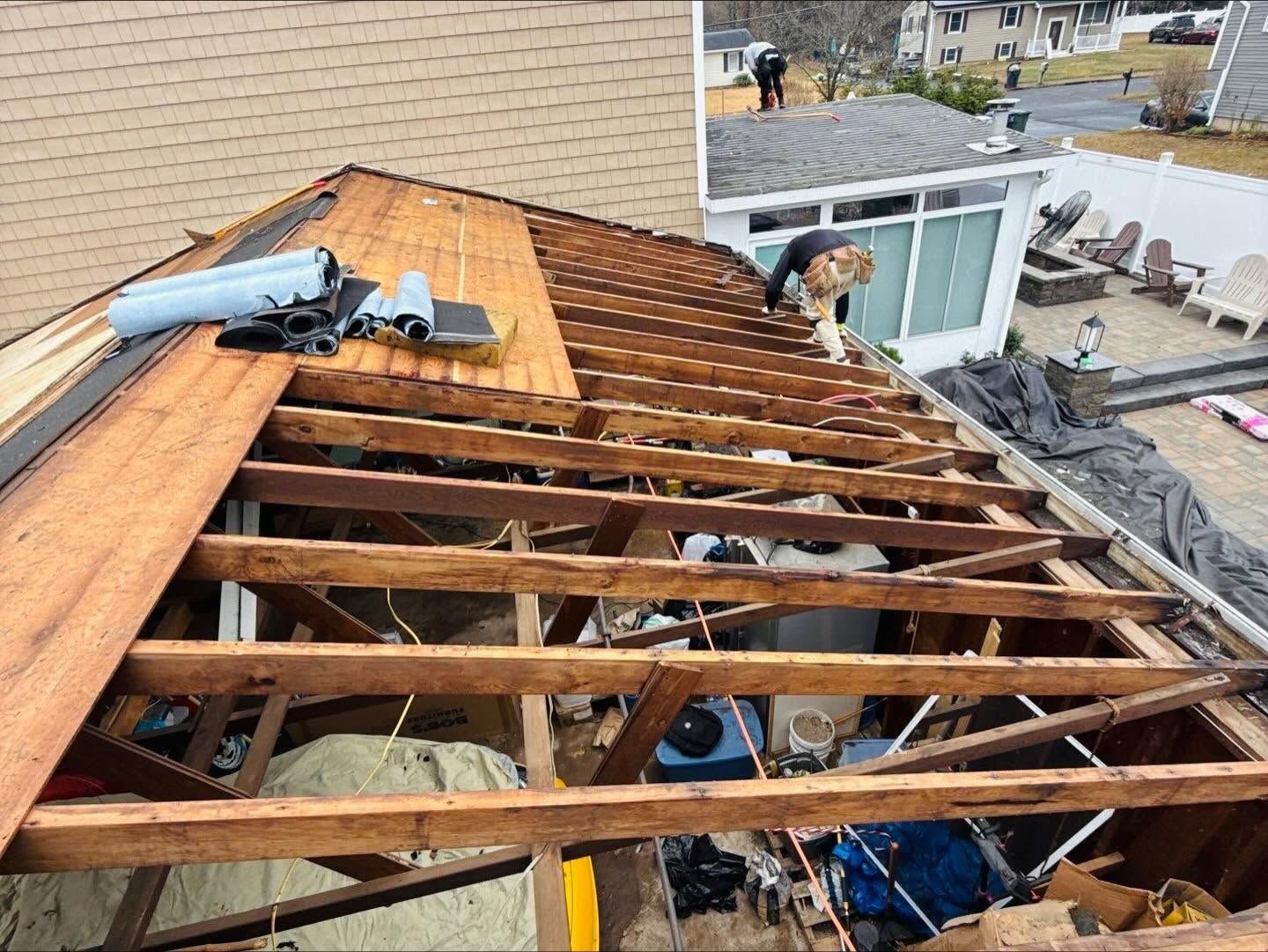 Roof under repair with exposed rafters, workers, and new plywood sheathing on a residential house