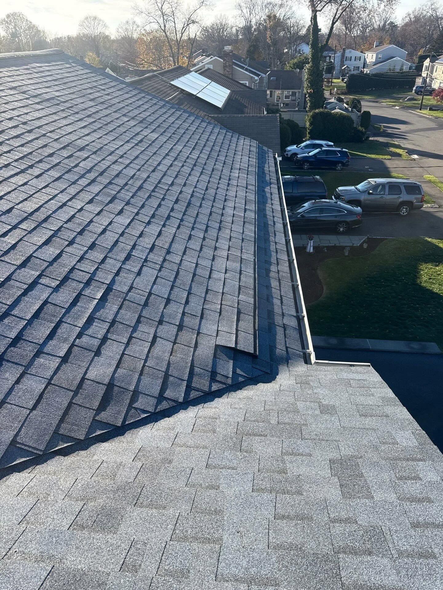 View from a roof with gray shingles over a parking lot and parked cars at sunset.