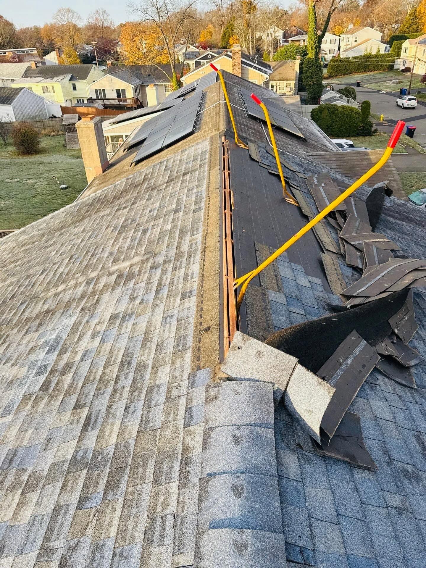 Damaged shingled roof with debris and exposed underlayment on a house rooftop.