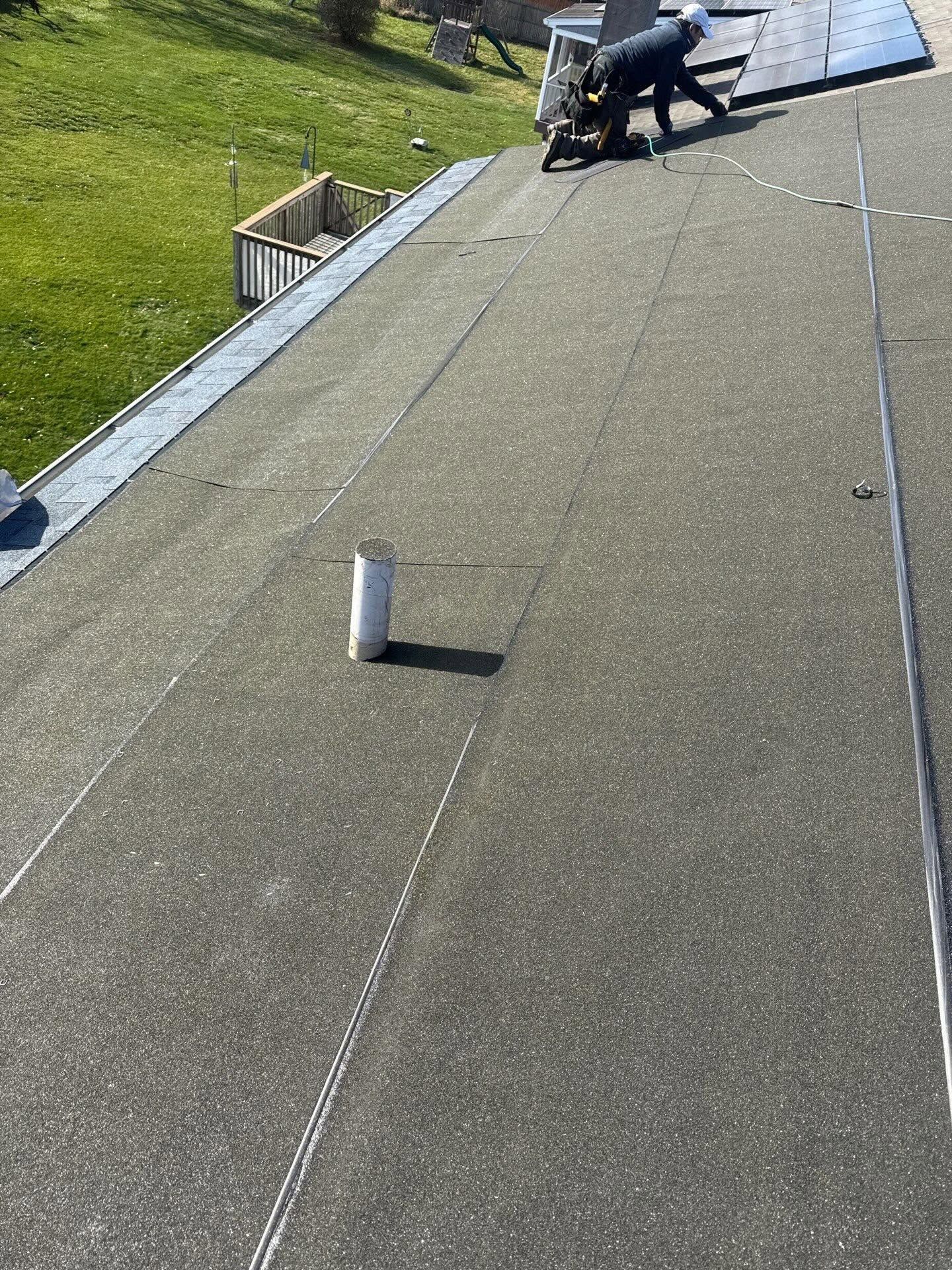 Two workers on a roof near a white vent pipe, with green lawn visible below.