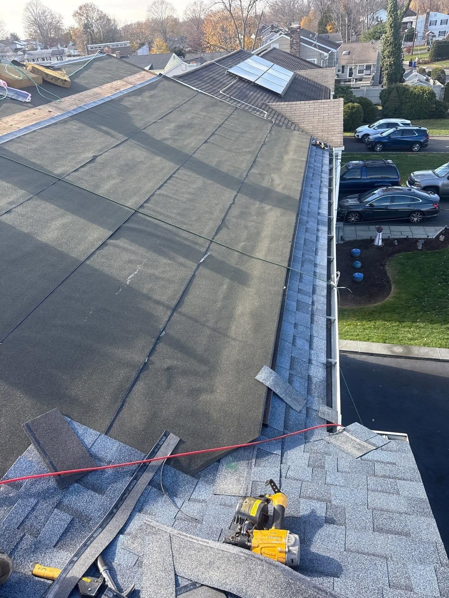Roofing work on a shingled house, with tools and materials near the roof edge.