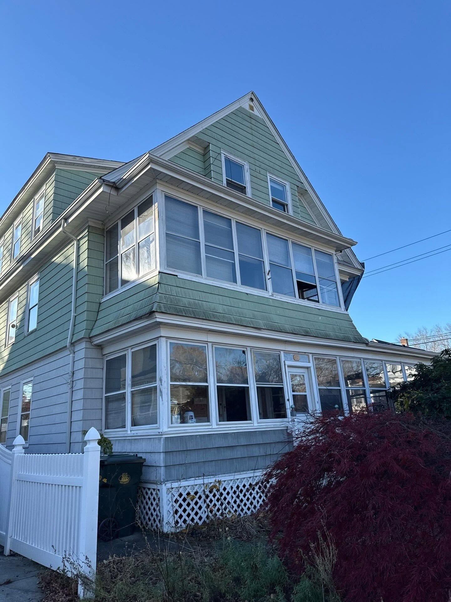 Three-story green house with white trim and sunroom under a clear blue sky