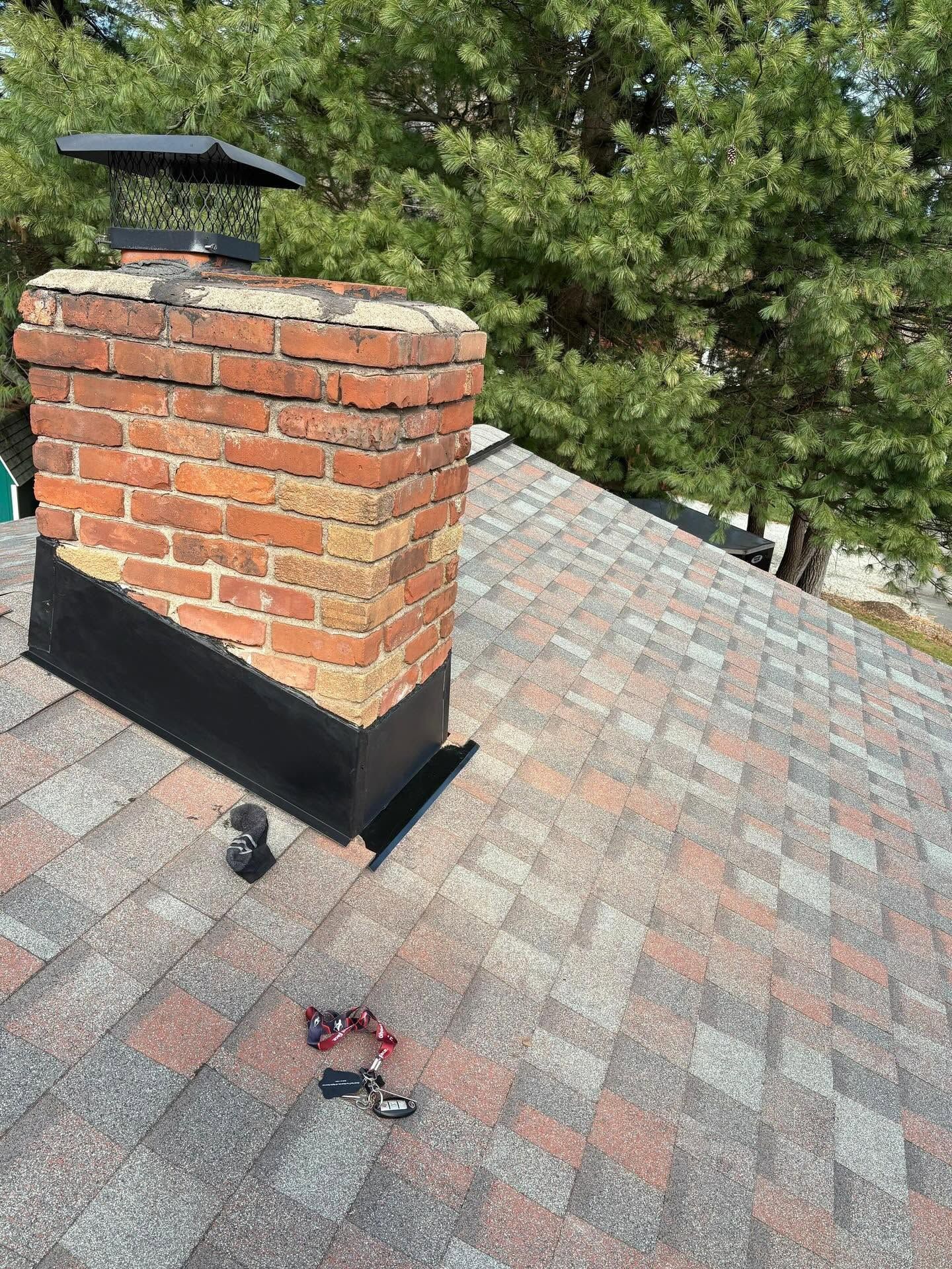 Brick chimney on a gray shingled roof with a damaged blue base flashing.