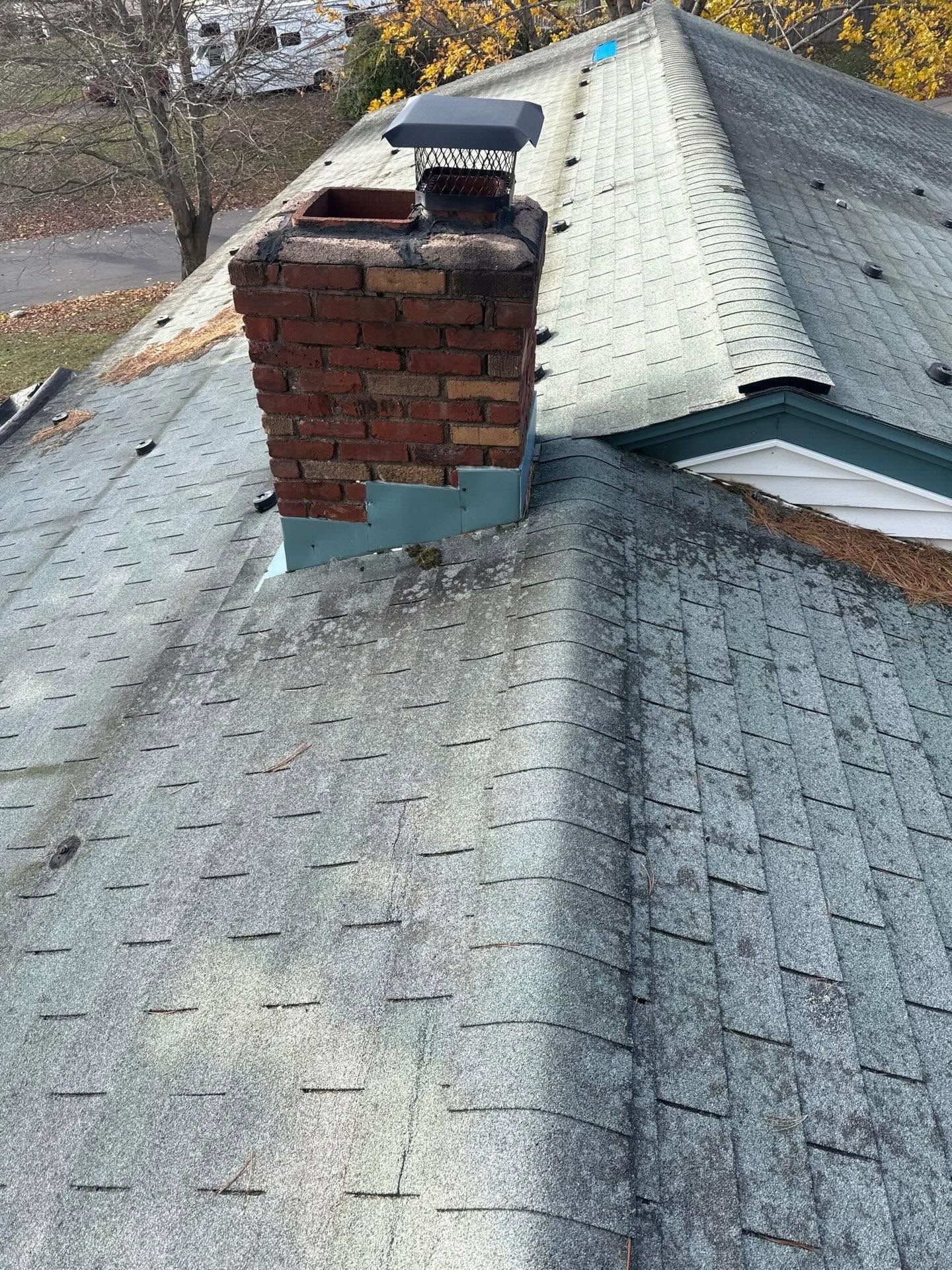 Roof with a brick chimney and metal cap on a gray shingled house.