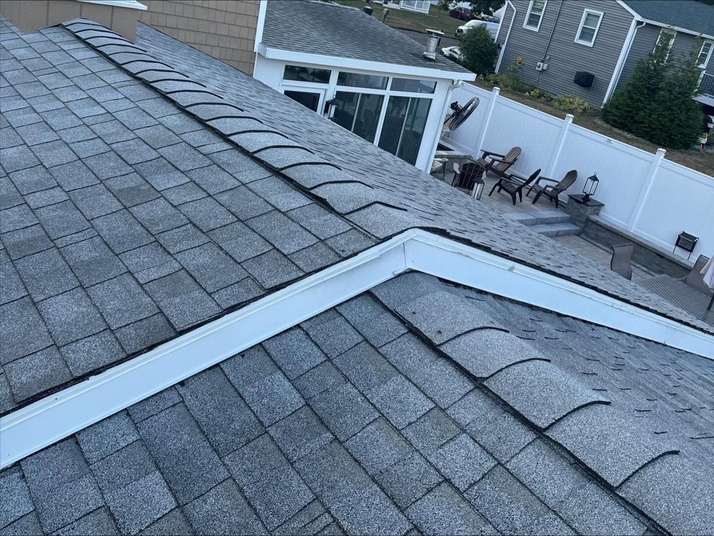 Rooftop with gray shingles and a white fence enclosing a patio with outdoor chairs.