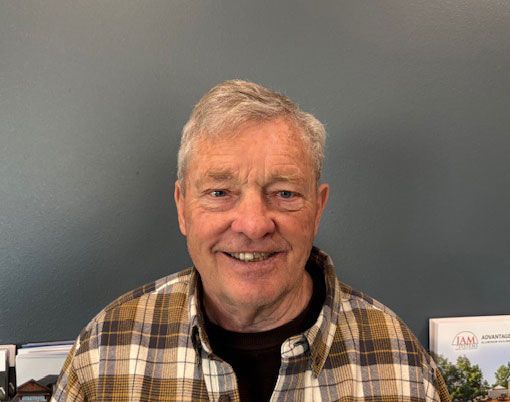Man with gray hair and a plaid shirt smiles at the camera in an office setting.
