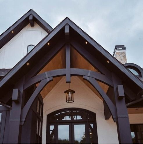 Dark stained wood entry with arched beams, lantern, and arched windows. White house with dark roof.
