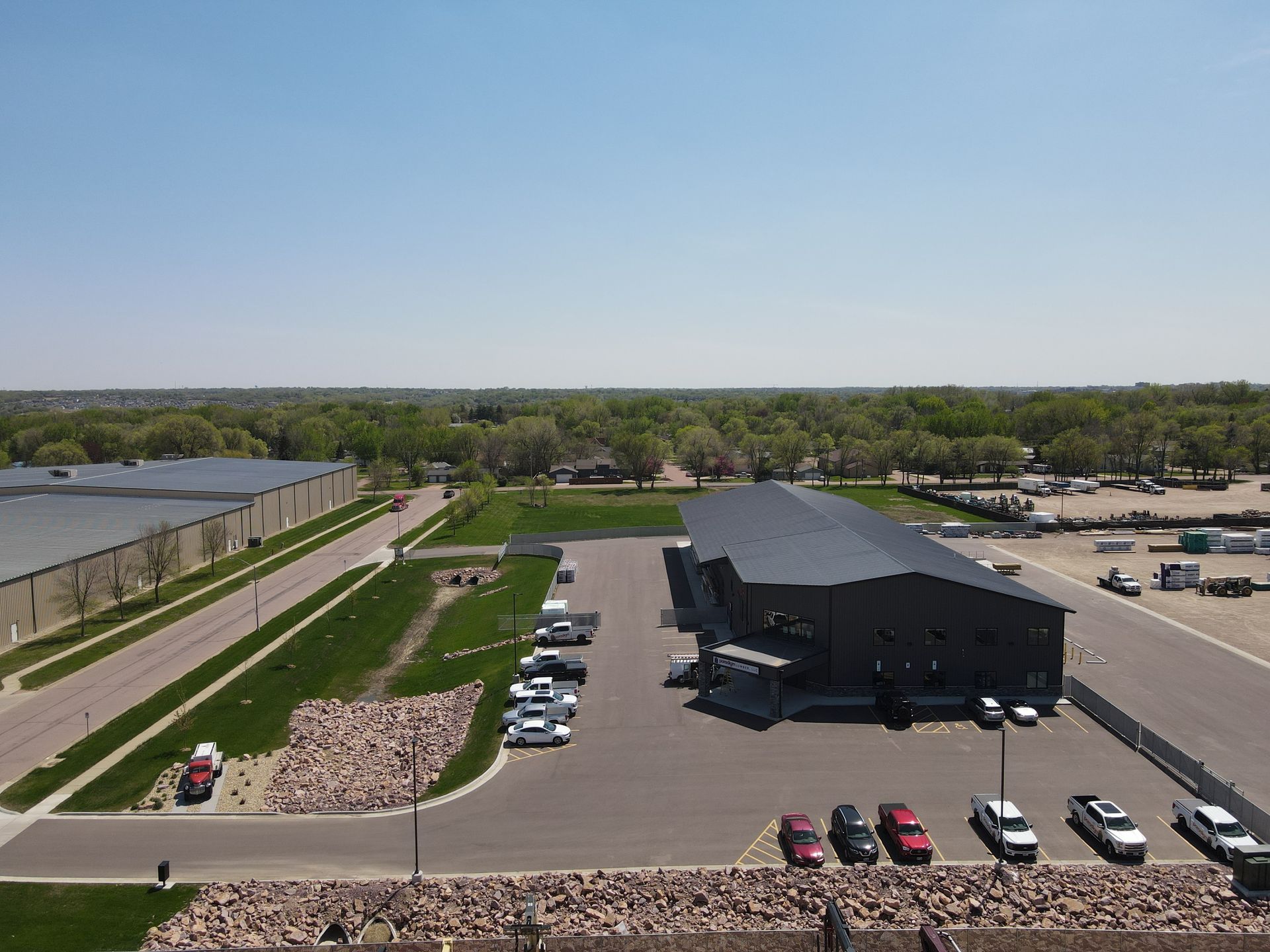 Aerial view of a modern industrial building with cars parked in the lot on a sunny day.