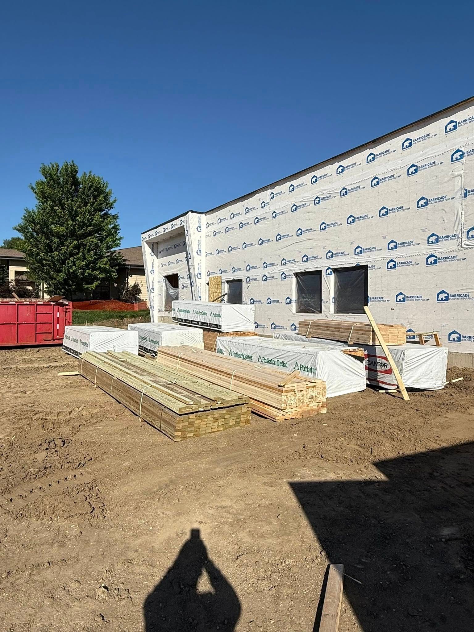 Construction site with building in progress; lumber and materials stacked outside; clear blue sky.