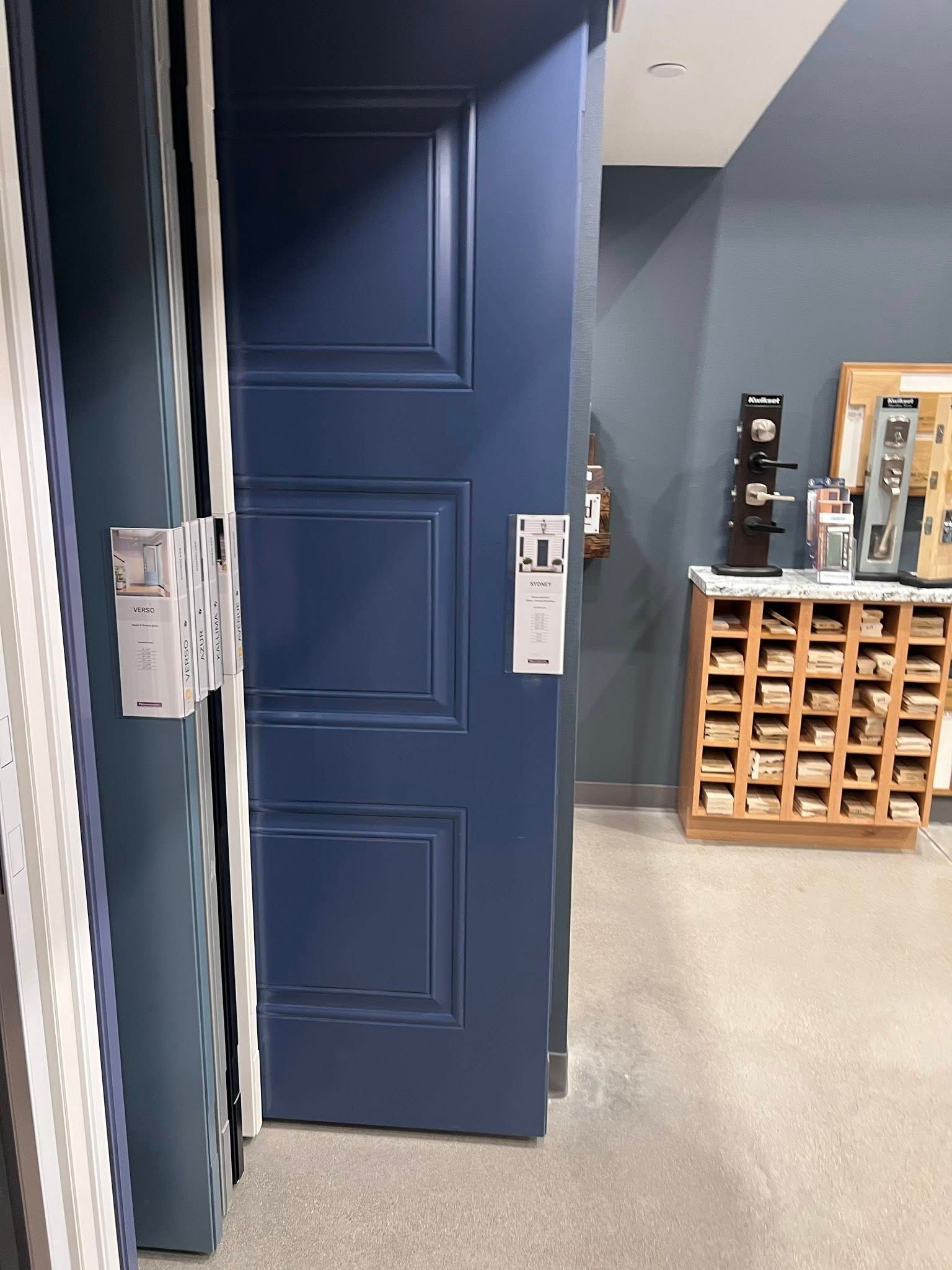 Blue paneled door in a showroom. White trim.  Displays of hardware in background.