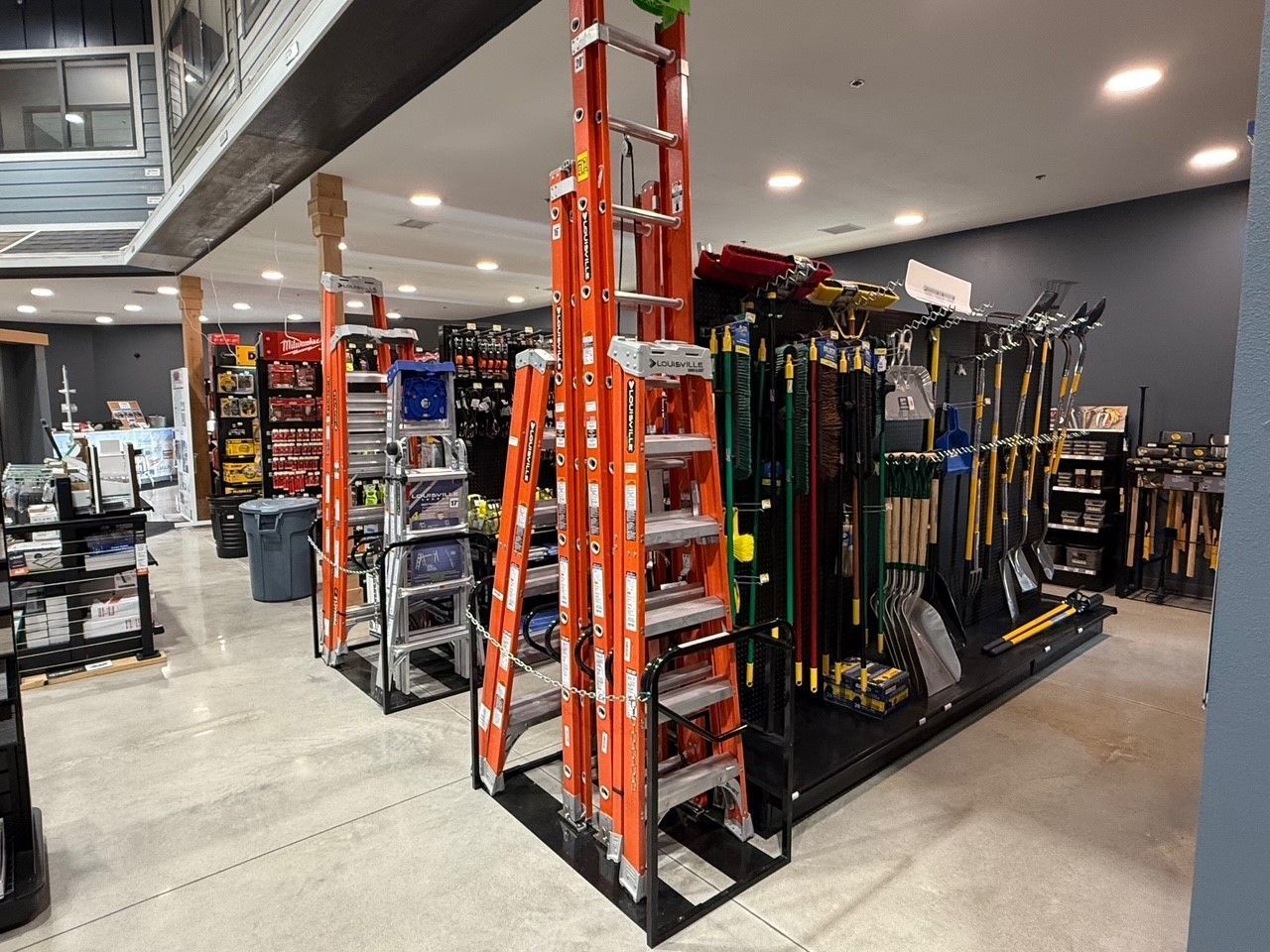 Inside a hardware store, orange ladders displayed on a rack, alongside tools and supplies.