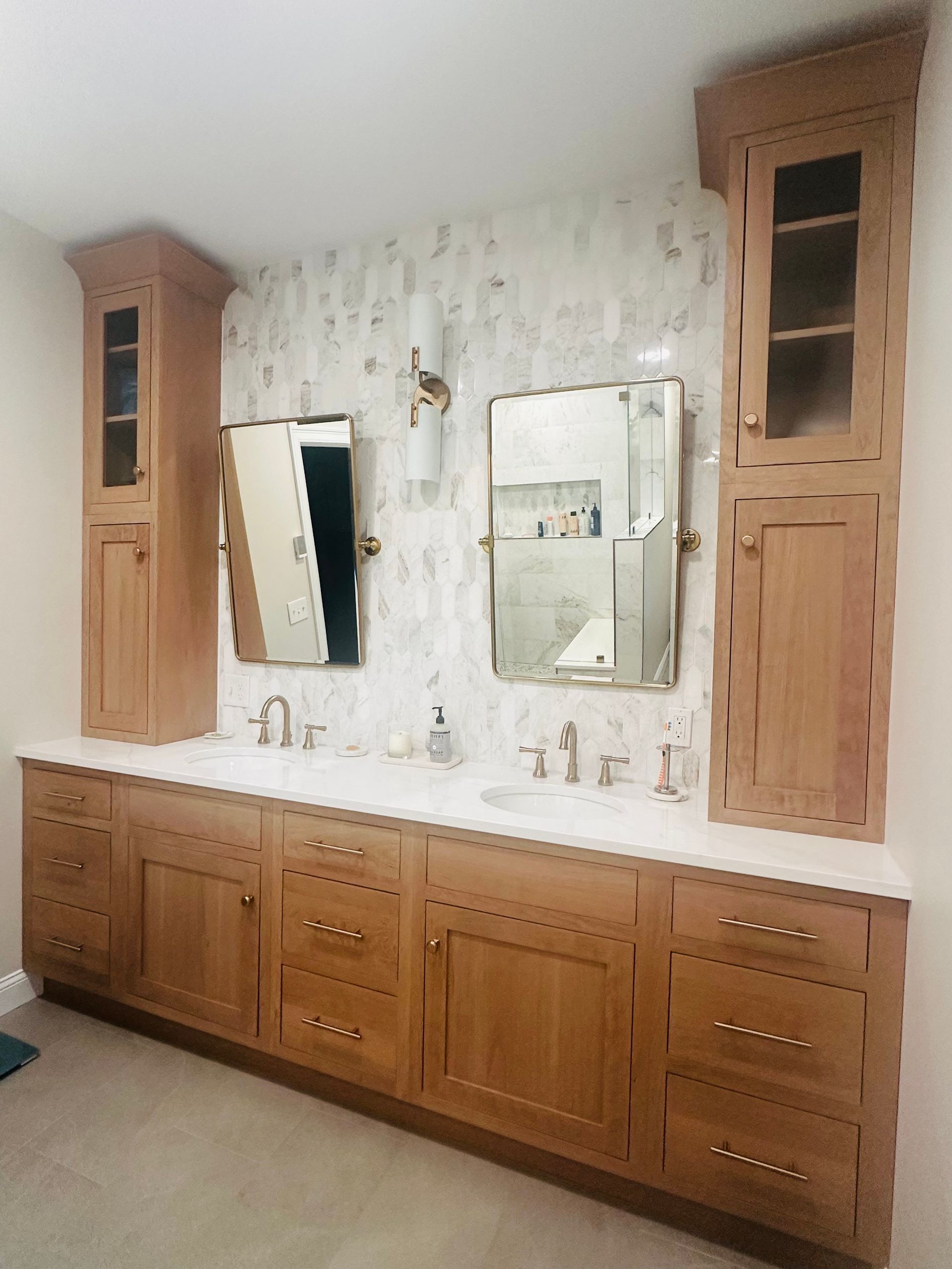 Wood bathroom vanity with double sinks, three mirrors, and tall wooden cabinets on either side.