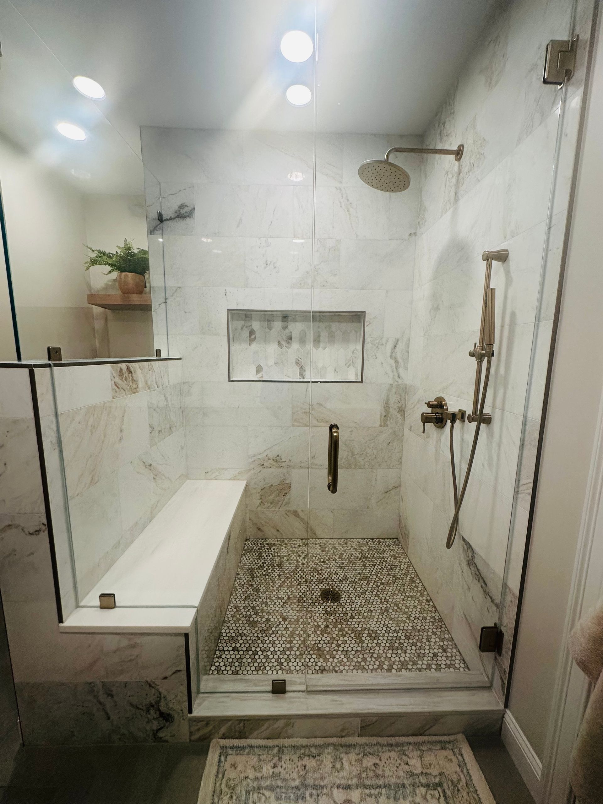 White tiled walk-in shower with bench, mosaic floor, wall niche, and handheld showerhead.