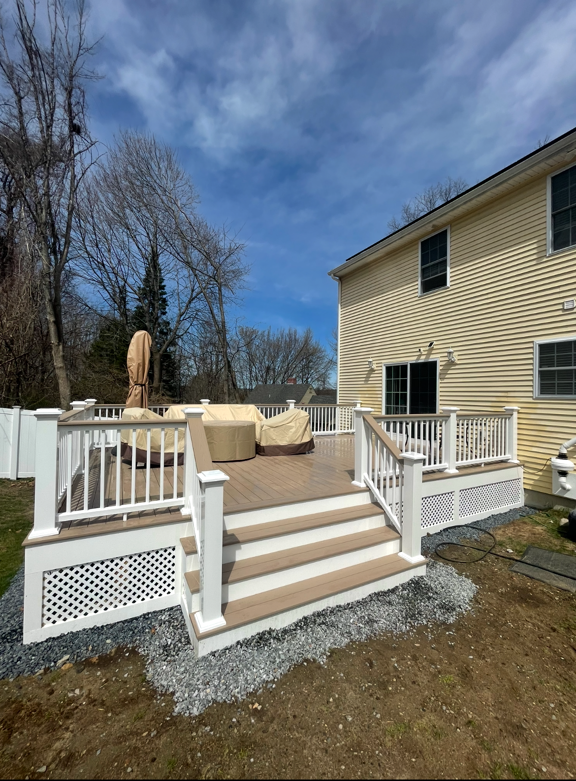 Backyard deck with white railings, tan steps, and beige house under a blue sky
