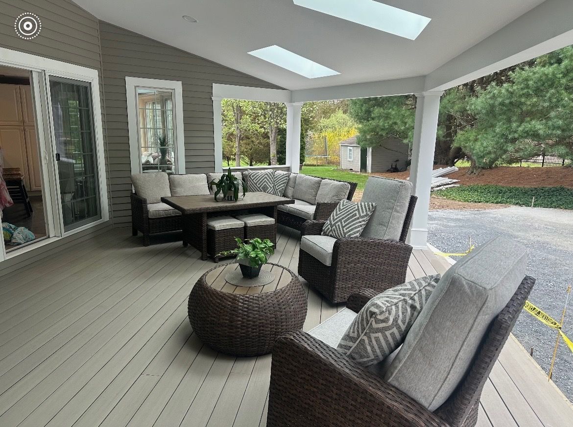 Covered patio with wicker seating, gray cushions, and a round coffee table overlooking a garden