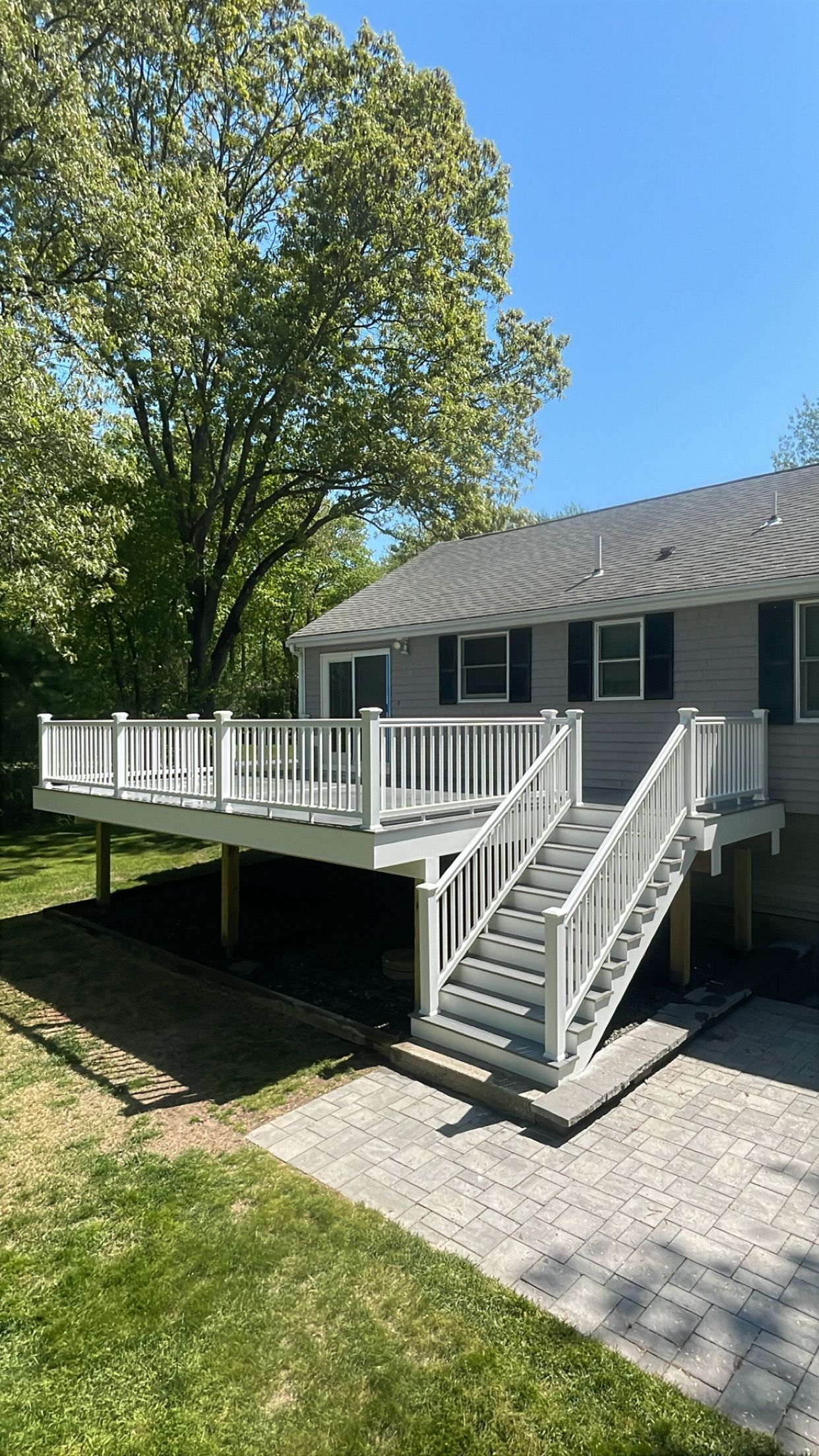 House with large white deck and stairs beside a tree on a sunny day