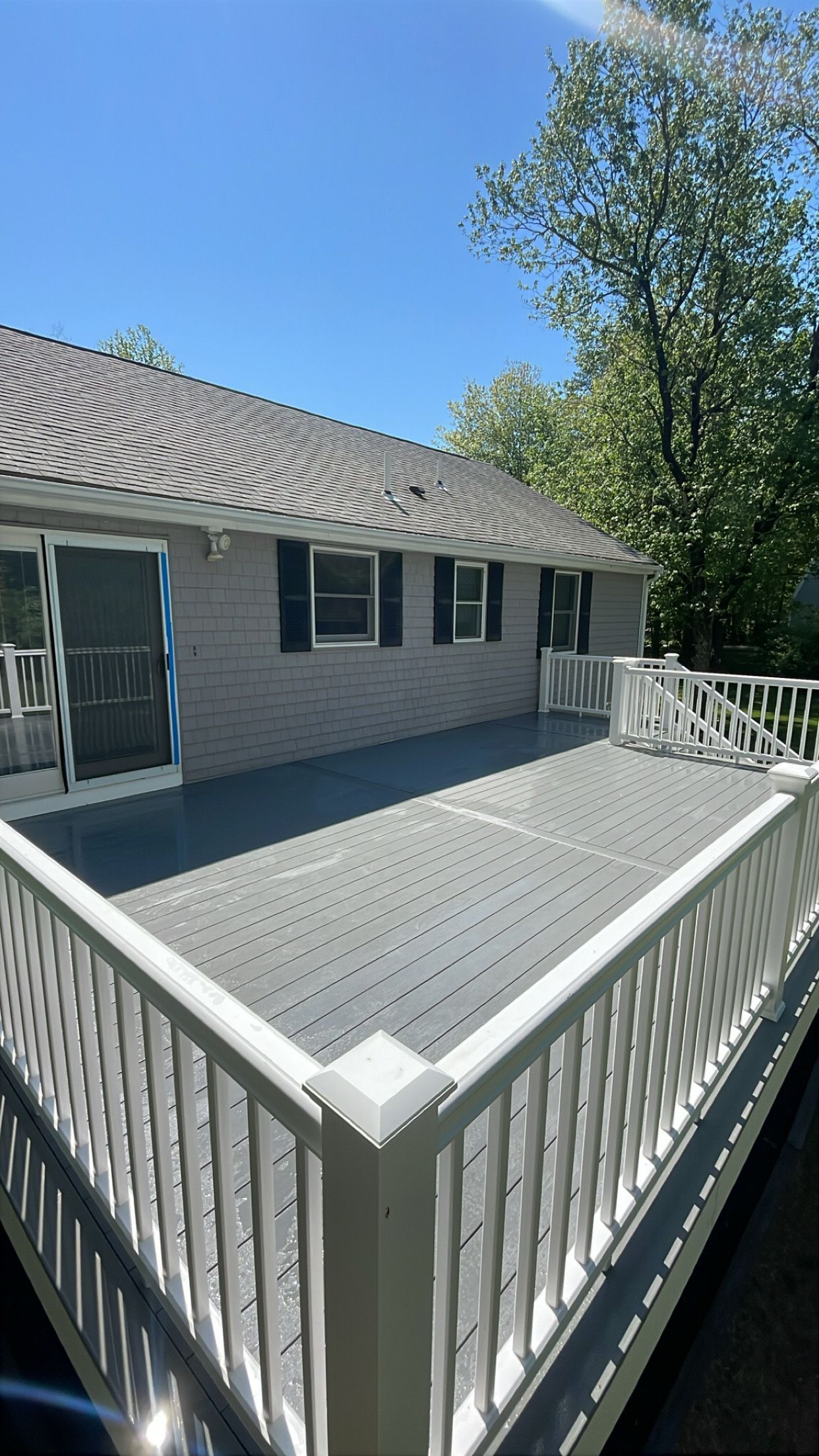 White wooden deck with railing beside a gray house under a bright blue sky.